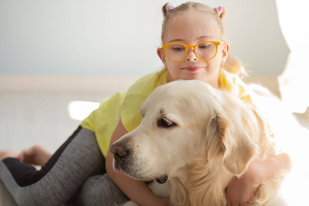 A girl with Down syndrome plays with dog Golden retriever in home - Foto, imagen