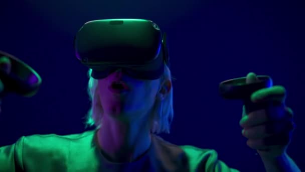 Energetic gamer playing online videogame with gamepads closeup. Active vr glasses man enjoying virtual reality with controllers. Blonde guy using joysticks for quest adventure game at neon light - Video