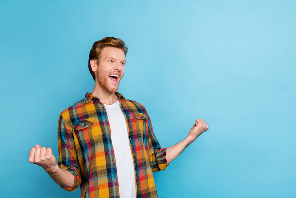Photo of cheerful handsome satisfied man with red hair dressed checkered shirt hold fists up shout yes isolated on blue color background. - Foto, Bild