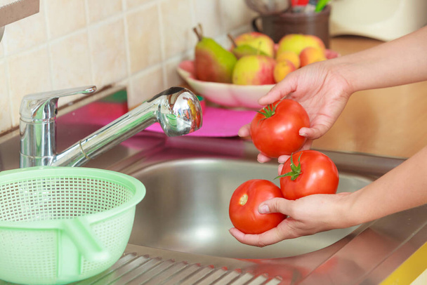 Woman hands washing fresh vegetables tomatoes in kitchen under water stream, preparation salad vegetarian meal - 写真・画像