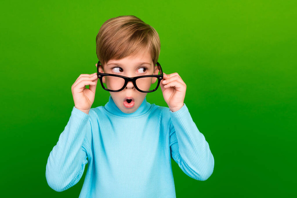 Photo of shocked funky small son wear turquoise turtleneck arms spectacles looking empty space isolated green color background. - Фото, изображение