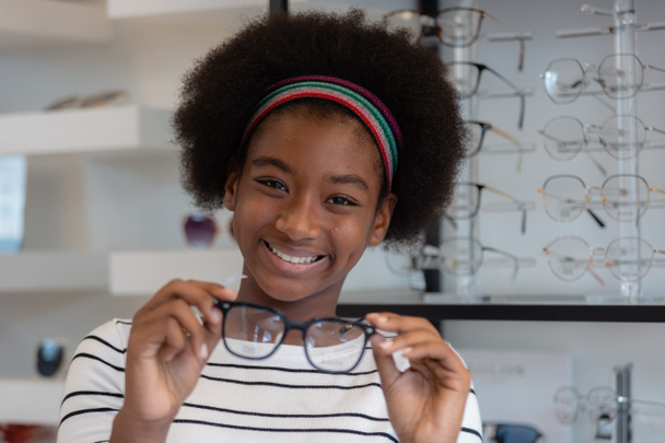 happy young woman African american afro hair smile holding spectacles standing at optical shop. modern ophthalmologist concept. - Photo, image