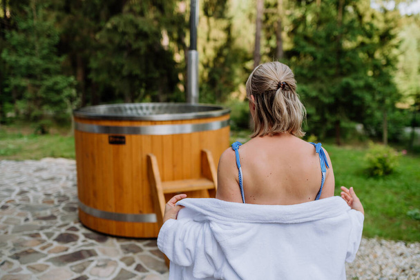 A young woman preapring to get into hot bath outdoors. Summer holidays in the mountains, hot water treatments and thermal spa concept, rear view. - Photo, image