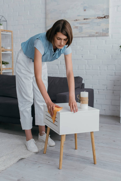 полная длина молодая брюнетка женщина уборка прикроватный столик на дому - Фото, изображение