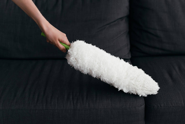 partial view of woman cleaning couch with dust brush - Foto, afbeelding