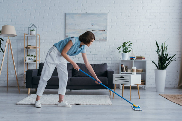 повна довжина жінки, що прибирає підлогу з мопедом у сучасній вітальні
 - Фото, зображення