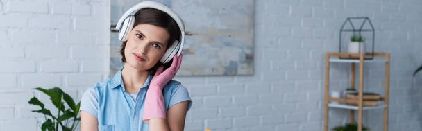 smiling housewife in rubber glove and wireless headphones looking at camera, banner - Foto, Bild