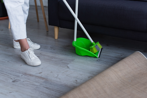 cropped view of woman in white sneakers near broom and scoop at home - Fotografie, Obrázek