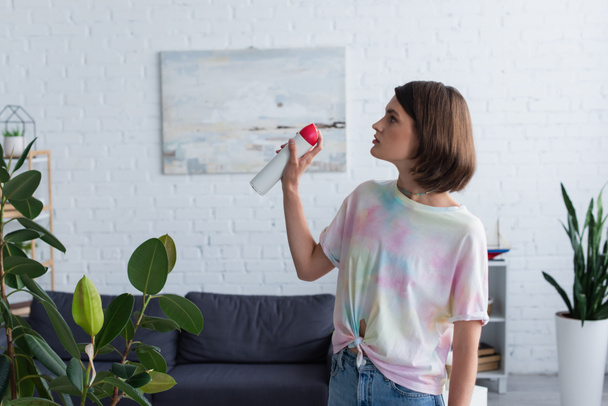 Side view of woman spraying air freshener in living room   - Foto, afbeelding