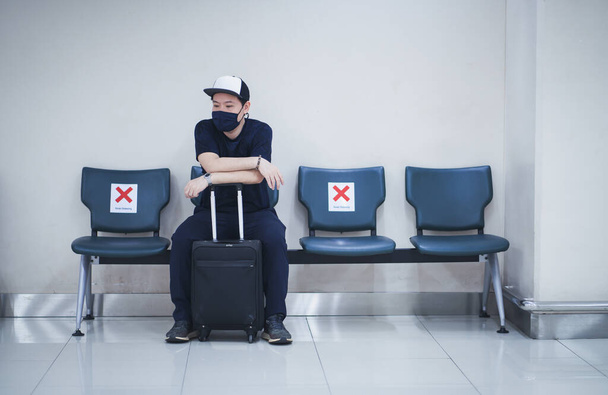Asian traveler wearing face mask sitting in an airport, Themes new normal, coronavirus and personal protection. - 写真・画像