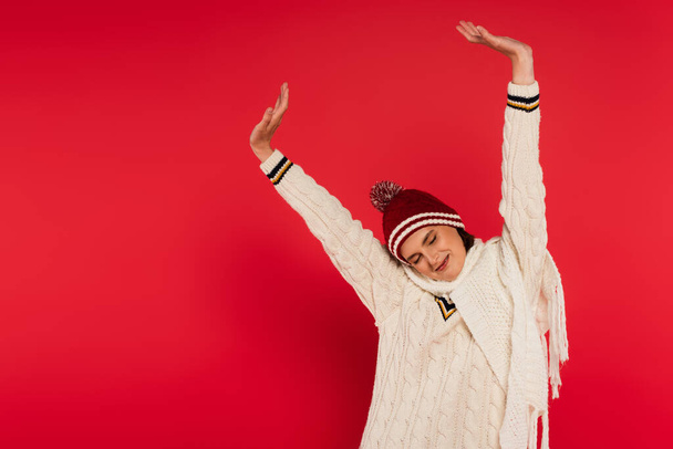 Cheerful woman in knitted clothes stretching on red background - Foto, immagini