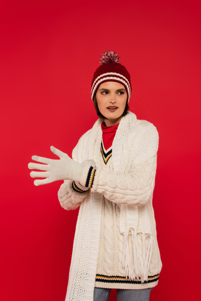 Young woman in warm clothes wearing gloves isolated on red  - Foto, Imagen
