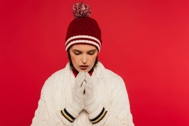 Woman in knitted clothes and gloves warming hands isolated on red  - Foto, Bild