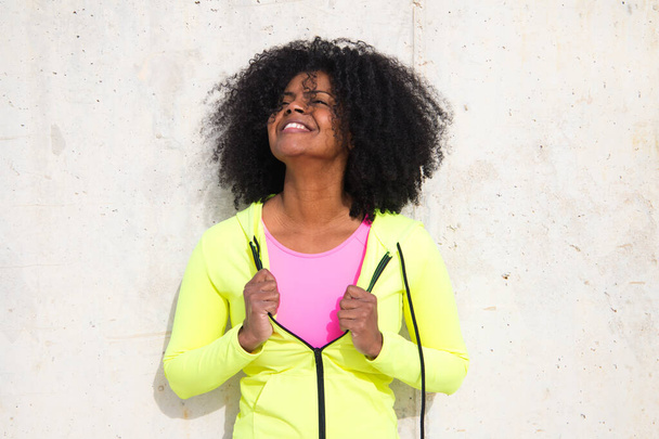 Красивая молодая афро-американка в ярко-зеленой и розовой спортивной одежде на сером бетонном фоне стены текстуры. У женщины другие выражения лица. Смеющиеся, серьезные, счастливые, грустные, думающие - Фото, изображение