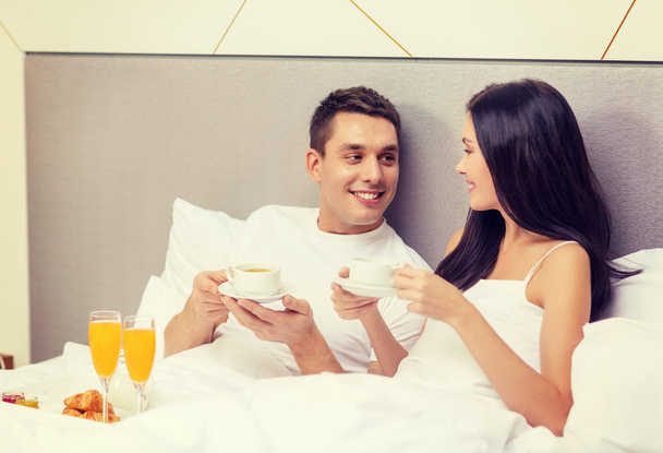 smiling couple having breakfast in bed in hotel - 写真・画像