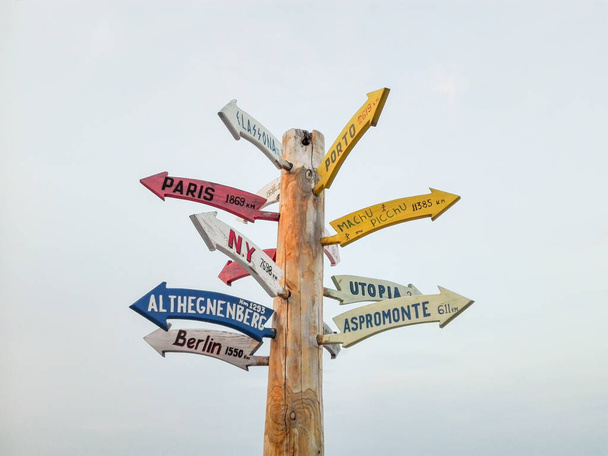 Wooden signpost in the public place. Signpost with directions to the cities. Travel destination choices on signpost. Wooden guidepost with colorful arrows with names of cities and places. - 写真・画像
