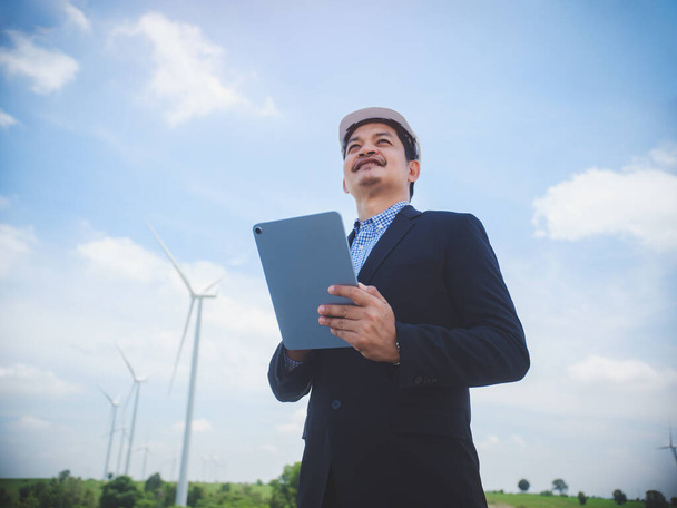 Successful engineer manager stand holding tablet front the wind turbines generating electricity power station. Concept of sustainability development by alternative energy - Φωτογραφία, εικόνα