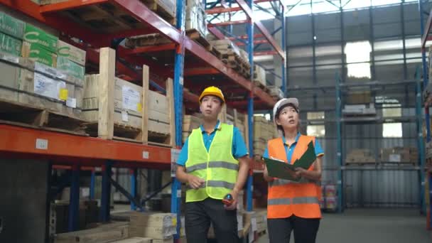 Warehouse workers asian team inspecting manufacturing storage. industrial colleagues in safety uniform and hardhat discussing distribution plan in large goods warehouse. - Video