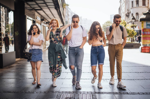 Group of cheerful young adults use a cellphone on a sumer city street. Concept of up to date lifestyle - Fotografie, Obrázek