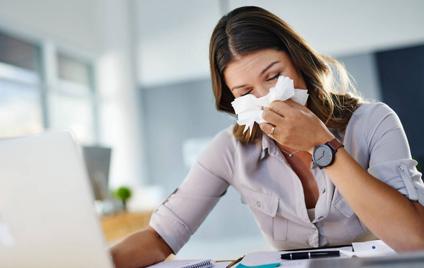 Having to blow my nose all the time is distracting. a businesswoman working in her office while suffering from allergies - 写真・画像