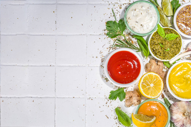 Assortment of different classic sauces and dips in sauceboats. Mayonnaise, ketchup, tartare, mustard, pesto, sour cream, barbecue sauces with spices, herbs, lemon - Photo, Image
