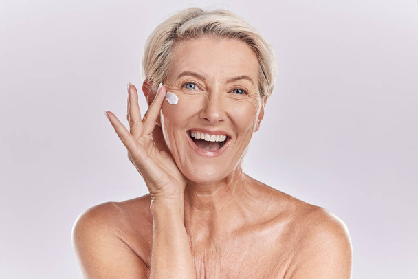 Skin, skincare or collagen lotion with old woman posing with a smile with her cosmetics and product. Senior female, facial cream and sunscreen for a healthy face and beauty model wellness portrait - Photo, image