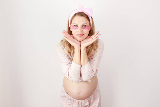 έγκυος γυναίκα με μπαλώματα και πιτζάμες σε λευκό φόντο - Φωτογραφία, εικόνα
