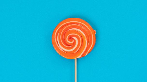 Round orange lollipop on a stick on a blue background - juicy sweet background. High quality photo - Foto, Imagem