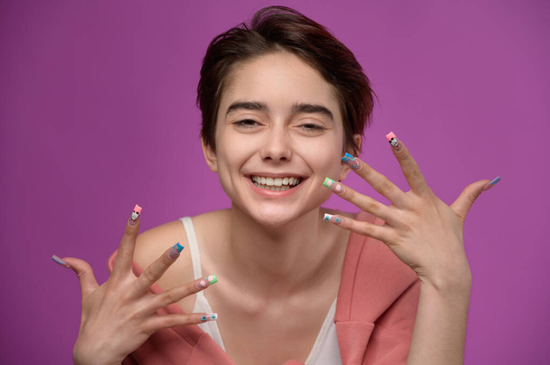 Affectionate cute girl with short haircut and extravagant nail art looking, studio portrait at colored background - Fotografie, Obrázek