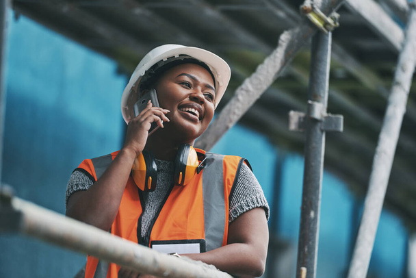 Construction manager, contractor and engineer talking on a phone while planning logistics at a building site in town. Happy, smiling and cheerful young female architect, supervisor and city planner. - Foto, imagen