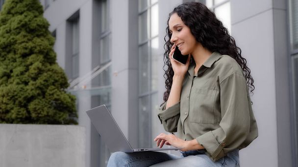 Busy multitasking businesswoman user freelancer worker lady sitting outdoor outside talking mobile phone typing laptop answer call ordering booking ecommerce shopping online with wireless computer app - Fotó, kép