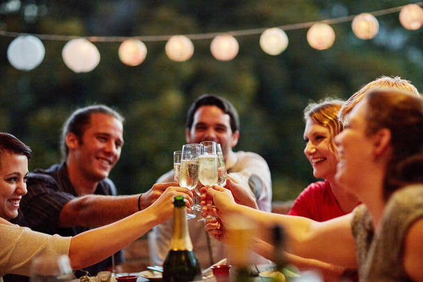 За дружбу. группа счастливых молодых друзей, пьющих шампанское на званом ужине во дворе - Фото, изображение