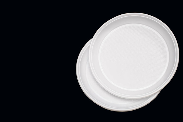 Disposable white plastic plates on a black background. Free space for text. Disposable plastic tableware for picnic or outdoor party. Plastic pollution and environmental problems - Photo, Image