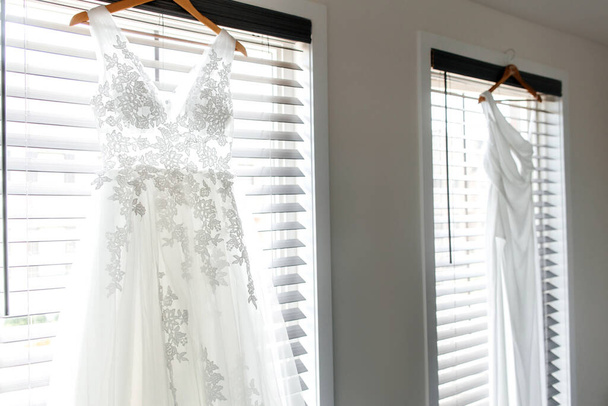 Bedroom with two women's wedding dresses for a lesbian LGBT wedding. Side view of beautiful white wedding dresses in a room against the background of windows for a same-sex wedding of two brides - Fotoğraf, Görsel