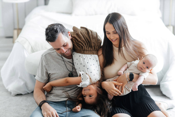 Happy young parents with their children play in the bedroom. Dad mom and their little daughter and newborn son. Happy family having fun with each other - Photo, image