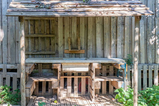 Wooden booth in neat and clean work area of a vegetable plot against wall of wooden planks, withe table, sink, sloping ceiling with remains of fallen branches, sunny summer day in an organic orchard - Fotó, kép