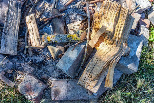 Close-up of an unlit campfire against gray and black extinguished ashes, stones surrounding wooden logs from tree trunks found in forest, moss, arranged in an irregular way, sunny day at campsite - Photo, Image