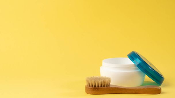 Een pot crème en een massageborstel op een gele achtergrond. Hoge kwaliteit foto - Foto, afbeelding