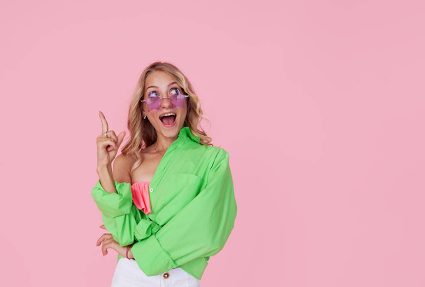 Have an idea. Portrait of pretty cheerful girl with wide open mouth in green bright shirt and star shape sunglasses isolated on pink  - Foto, immagini