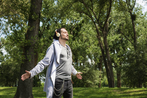 Безтурботний чоловік з простягнутими руками насолоджується свободою і слухає музику через навушники
. - Фото, зображення