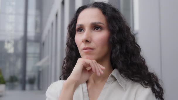 Close up pensive thoughtful puzzled Caucasian Hispanic thoughtfully girl woman with curly hair standing outdoors sad worry dreaming planning businesswoman thinking about idea solution problem thought - Filmati, video