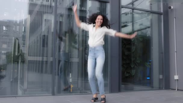 Funny 30s woman success businesswoman lady with long curly hair having fun outdoors alone jumping high in air near office company building flying jump active movement celebrate happy victory winning - Video, Çekim
