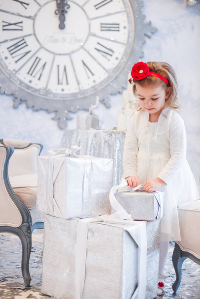 fille dans une robe blanche élégante délier ruban sur cadeau de Noël enveloppé dans du papier cadeau léger. Fille sur le fond de l'horloge montrant minuit. Contexte de la carte de voeux du Nouvel An - Photo, image