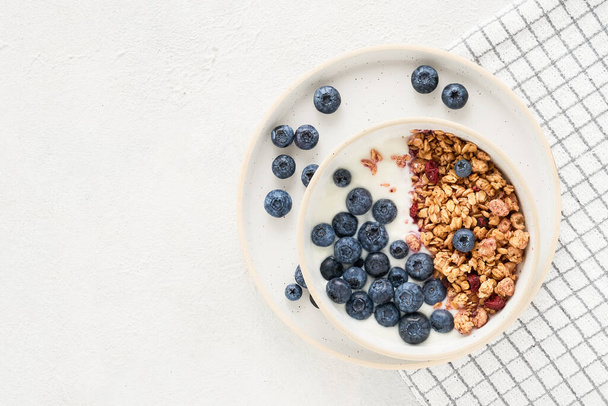 Bowl of homemade yogurt with granola and blueberries on a light background. Top view, copy space for text - Photo, Image
