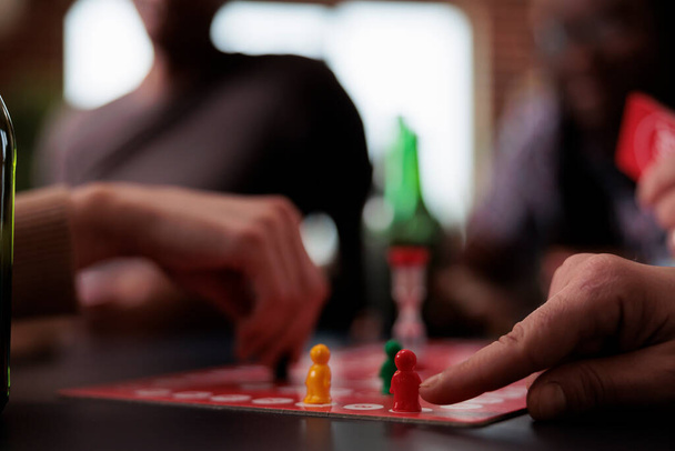 Close up of people hands moving plastic figurines on game table while sitting at table. Group of friends playing boardgames together while enjoying snacks and cold beverages. - Photo, image