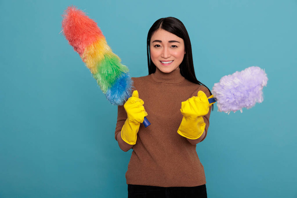 Optimistic joyful and smiling asian young housemaid from homework holding two duster brush in yellow gloves, Cleaning home concept, smiling female ready for his duty, Housewife feeling glad satisfied - Foto, afbeelding