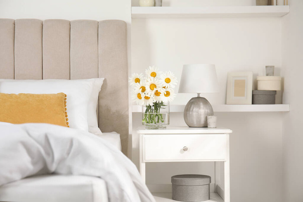 Bouquet of beautiful daisy flowers and lamp on nightstand in bedroom - Fotografie, Obrázek