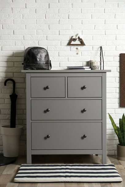 Grey chest of drawers near white brick wall indoors - Zdjęcie, obraz