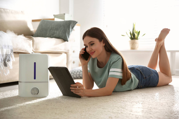 Woman using gadgets in room with modern air humidifier - Foto, Bild