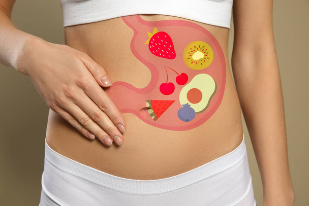 Woman with image of stomach full of food drawn on her belly against beige background, closeup. Healthy eating habits - Valokuva, kuva